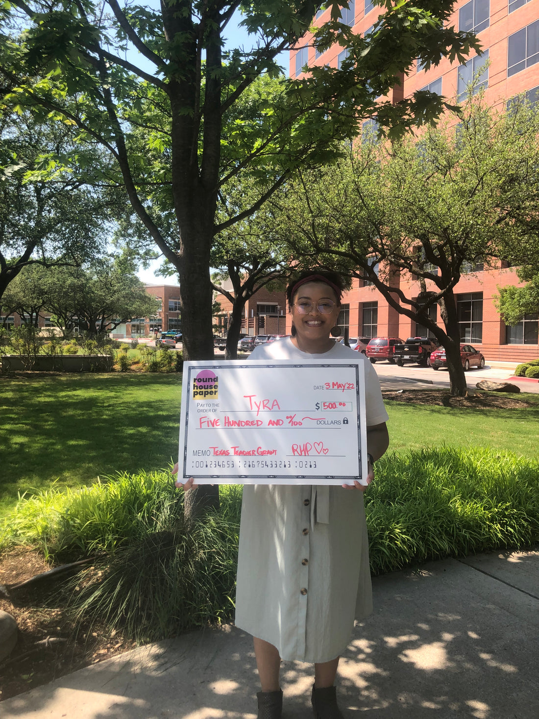 Woman holds 500 dollar promotional check for Round House Paper 1st Annual Texas Teacher Grant